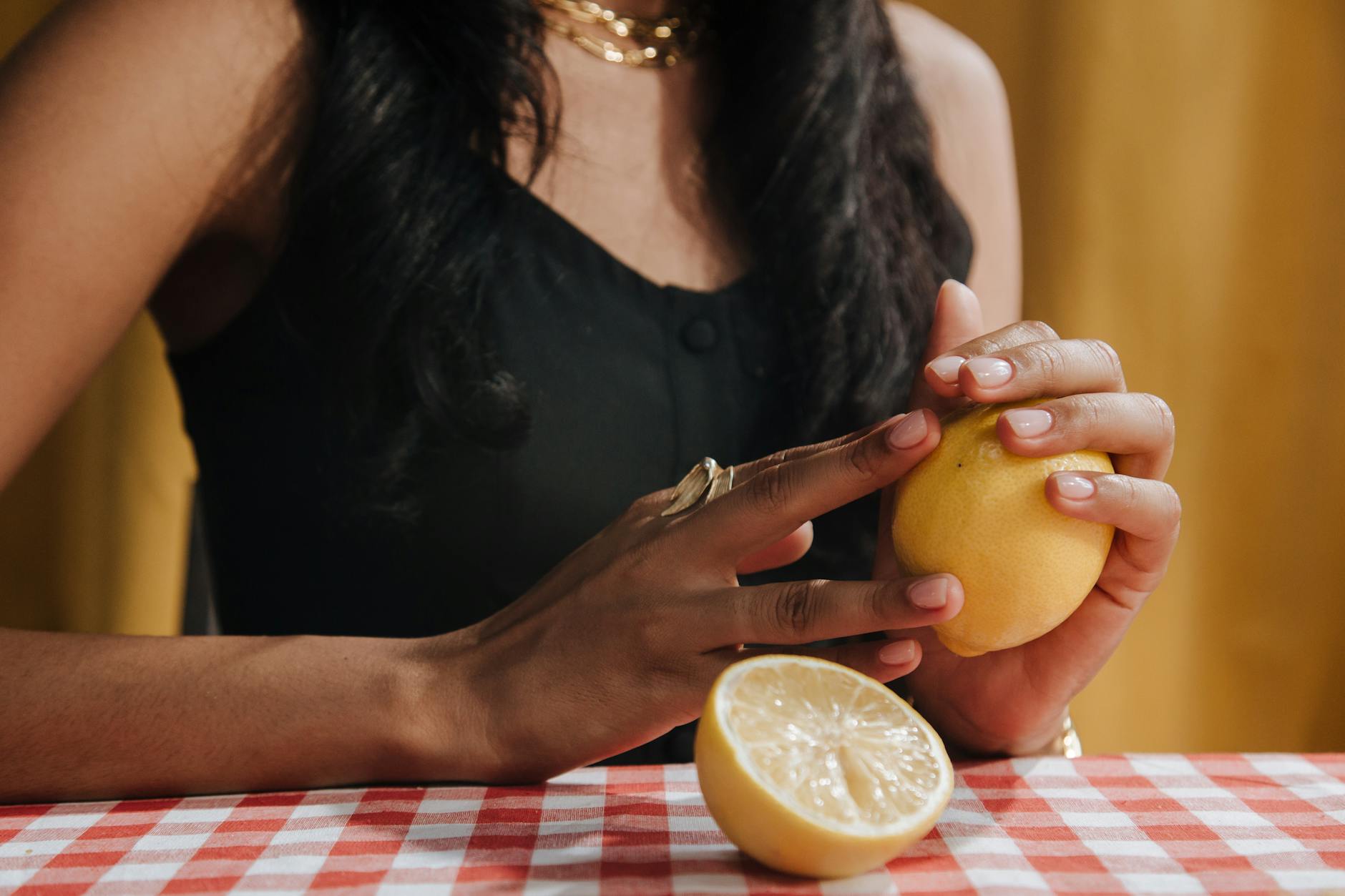 A woman holding a fresh lemon at a dining table, symbolizing the citrus-inspired design of the lemon vibrator