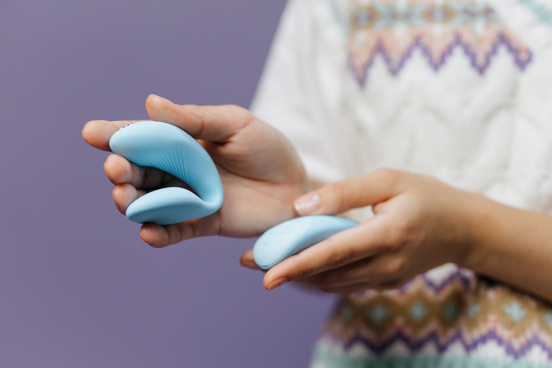 Close-up of hands holding a sleek blue vibrator against a purple background, representing intimate partner connection.