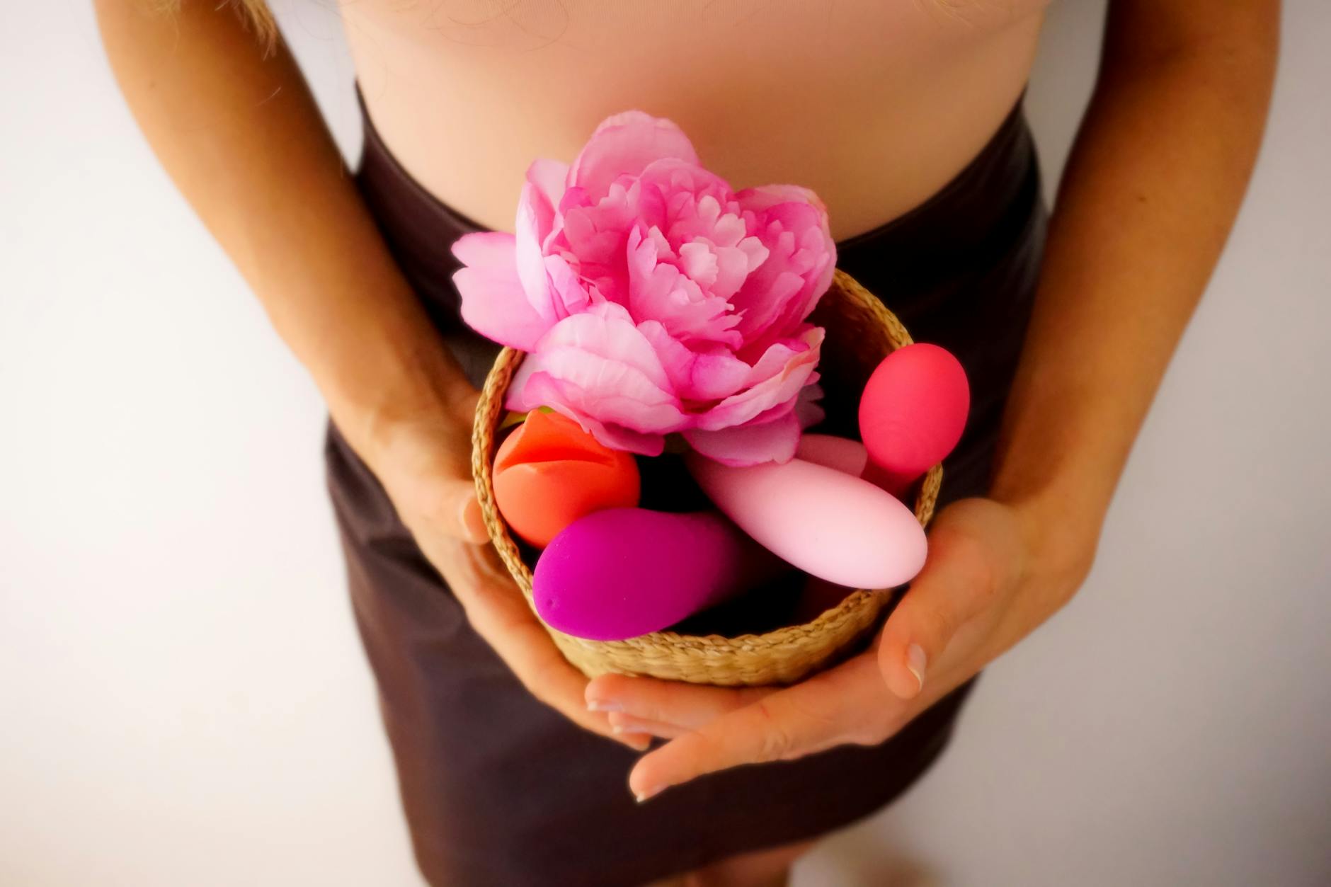A basket of colorful vibrators including lemon-shaped toys on a white background with pink flowers